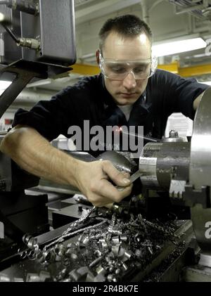 US Navy Machinery Servicebetrieb Klasse 3. misst den Umfang eines Lochs, das mit einer Drehmaschine in massiven Stahlwerkstoff gebohrt wird. Stockfoto