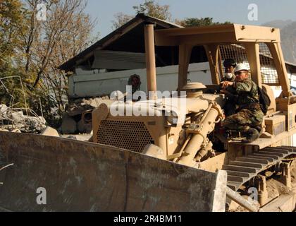 US Navy USA Navy Senior Chief Construction Mechanic Right, weist Maschinenführer 3. Klasse an, welcher Teil der Technischen Universität in Muzaffarabad als Nächstes entfernt werden soll. Stockfoto