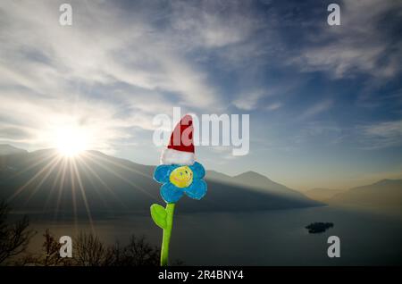 Lächeln Sie mit Weihnachtsmütze und Sonnenschein über dem alpinen Lago Maggiore mit Brissago Islands und Mountain in Ticino, Schweiz Stockfoto