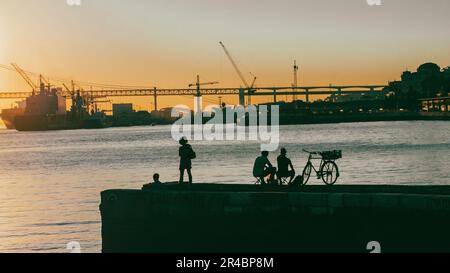 Eine Gruppe von Menschen, die den atemberaubenden Sonnenuntergang vom Ende eines Piers auf dem Tejo in Lissabon bewundern Stockfoto