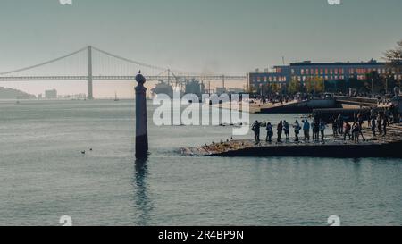 Eine Gruppe von Menschen, die den atemberaubenden Sonnenuntergang vom Ende eines Piers auf dem Tejo in Lissabon bewundern Stockfoto