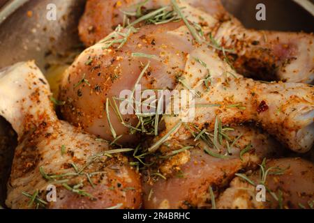 Rohe Hühnerschenkel mit Gewürzen. Mariniertes Huhn mit Rosmarin und Paprika. Rohes Fleisch. Rohes Fleisch in der Schüssel. Hausgemachtes Barbecue. Fleisch und Kräuter. Stockfoto