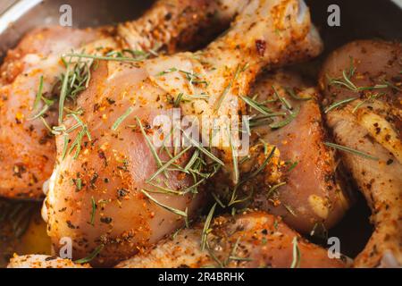 Rohe Hühnerschenkel mit Gewürzen. Mariniertes Huhn mit Rosmarin und Paprika. Rohes Fleisch. Rohes Fleisch in der Schüssel. Hausgemachtes Barbecue. Fleisch und Kräuter. Stockfoto