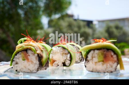 Ein weißer Teller mit einer Vielzahl von Sushi-Brötchen, garniert mit farbenfrohem Gemüse Stockfoto