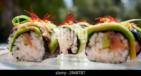Ein weißer Teller mit einer Vielzahl von Sushi-Brötchen, garniert mit farbenfrohem Gemüse Stockfoto