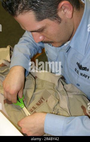 US Navy Petty Officer 2. Class schneidet sein neu ausgestelltes Desert Camouflage Uniform Top. Stockfoto
