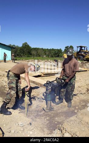 US Navy USA Navy Seabee Builder Construction misst die Grabentiefe, während der Bauelektriker der Klasse 3. den verrückten Packer betreibt. Stockfoto