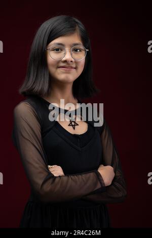 Ein Porträt einer jungen Inderin, die eine Brille auf einem leuchtend roten Hintergrund trägt Stockfoto
