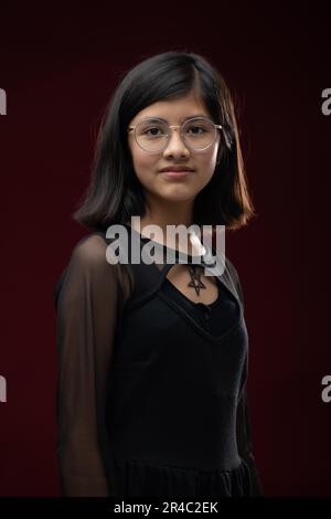 Eine reife Frau, die eine Brille trägt und von der Kamera wegschaut, während sie vor einem hellroten Hintergrund steht Stockfoto