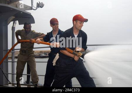 MATROSEN DER US Navy, die an Bord des U-Boot-Tenderschiffs USS Emory S. Land (AS 39) eingesetzt wurden, und Mitglied der kongolesischen Militärpraxis für die Handhabung von Löschschläuchen. Stockfoto