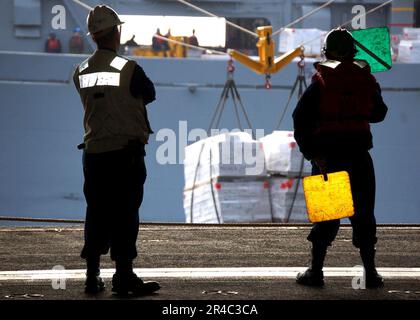 US Navy Ein an Bord des Flugzeugträgers USS Abraham Lincoln (CVN 72) der Nimitz-Klasse stationierter Signalgeber signalisiert, dass das Schiff während einer laufenden Wiederauffüllung Vorräte erhält. Stockfoto