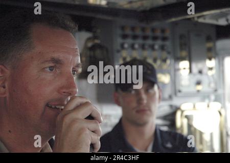 KOMMANDANT der US Navy USS Lake Champlain (CG 57), Captain, verwendet die 1MC-Lautsprecheranlage, um die Crew von der Brücke aus anzusprechen, während Quartermaster 3. auf uns zusieht. Stockfoto