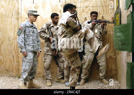 US Navy ein Soldat der irakischen Armee, vom 5. Bataillon, tritt eine Tür ein, innerhalb des Tötungshauses, während die Army SPC, Hauptquartier-Kompanie, 1. Bataillon, 327. Infanterie-Regiment beobachtet. Stockfoto