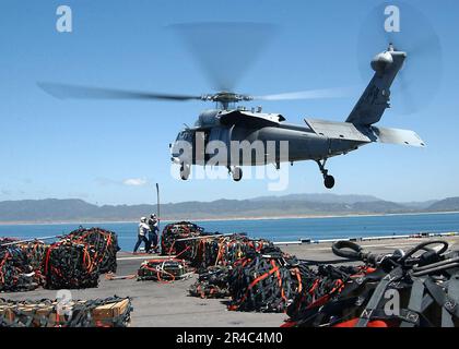 US Navy zwei Matrosen bereiten sich darauf vor, einen Frachtanhänger an einem MH-60s Seahawk Helikopter zu befestigen, während sie Waffen auf das Cockpit an Bord des Amphibienschiffs USS Tarawa (LHA 1) abladen. Stockfoto