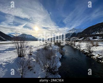 Eine ruhige Winterszene mit einem Fluss, der sich durch eine schneebedeckte Landschaft mit einer majestätischen Bergkette im Hintergrund schneidet Stockfoto