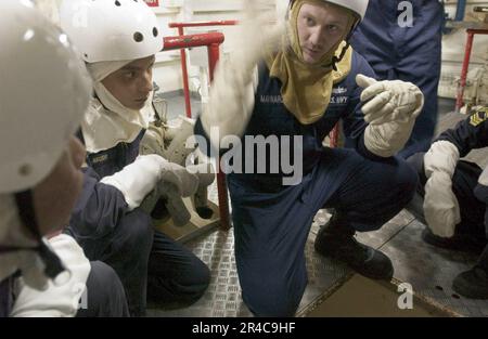 US Navy Damage Controlman 3. Class erklärt einer Gruppe von Seeleuten der Republik Singapur in einem kombinierten Schadenskontrollszenario, wie man Überschwemmungen kontrolliert. Stockfoto