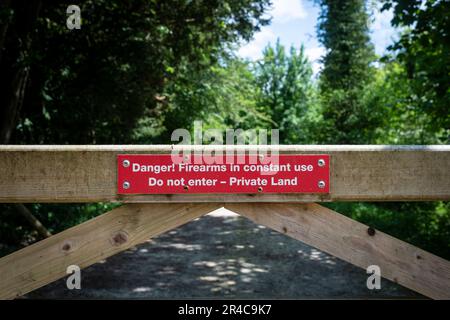 Rotes Warnschild an einem Tor „Gefahr! Schusswaffen im Dauereinsatz. Nicht betreten - Privates Land“. Stockfoto