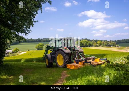 Traktor auf einem Feld, der langes Gras am Feldrand schneidet. Stockfoto