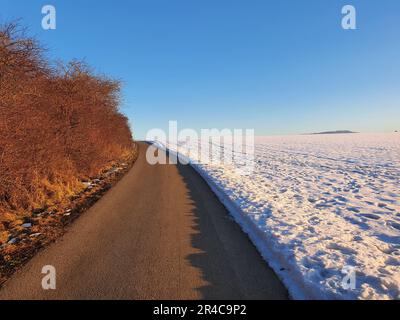 Eine Winterszene mit einer langen, kurvenreichen schneebedeckten Straße, die sich bis zum Horizont erstreckt und eine surreale und geheimnisvolle Atmosphäre bietet Stockfoto