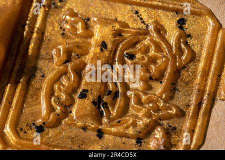 Ein goldenes Metallic-Kunstwerk mit einem aufwendigen Blumenmuster und zwei kleineren schwarzen Punkten Stockfoto