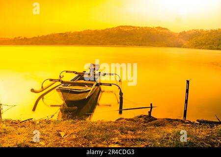 Traditionelles Boot am ruhigen und ruhigen See während des Sonnenaufgangs am Jatibarang-Staudamm, Semarang, Indonesien. Stockfoto