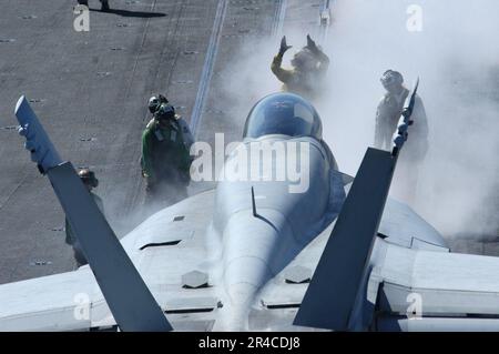 US Navy ein Flugzeugdirektor leitet eine F-A-18F Super Hornet, die dem Strike Fighter Squadron One Zero Two (VFA-102) zugeteilt wurde, in Position für den Start vom Flugdeck der USS Kitty Hawk (CV 63). Stockfoto