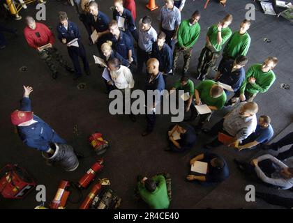 US Navy Damage Controlman Klasse 3. erklärt die Feuerlöschausrüstung während der grundlegenden Schulung zur Schadensbegrenzung in der Hangarbucht des nuklearbetriebenen Flugzeugträgers USS Enterpris. Stockfoto