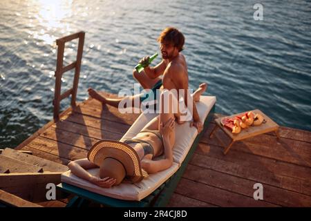 Ein Blick aus der Vogelperspektive auf ein junges Paar im Badeanzug, das an einem wunderschönen Sommertag am Flussufer plaudert und sich sonnt. Sommer, Fluss, Urlaub Stockfoto