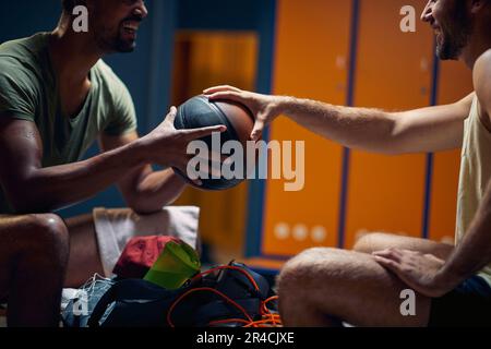Zwei junge Spieler sitzen von Angesicht zu Angesicht auf einer Bank und halten Basketball. Ich bereite mich auf das Training vor. Stockfoto