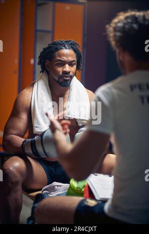 Junger Boxspieler sitzt in der Garderobe von Angesicht zu Angesicht und der Trainer spricht. Beratung nach dem Training. Stockfoto