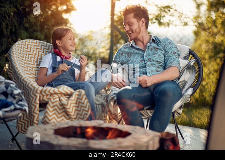 Der Moment der reinen Verbindung und der Liebe zwischen einem Vater und seiner Tochter. Sie teilten die Erfahrung, wie Marshmallows geröstet wurden, wird zum Symbol des Schatz Stockfoto