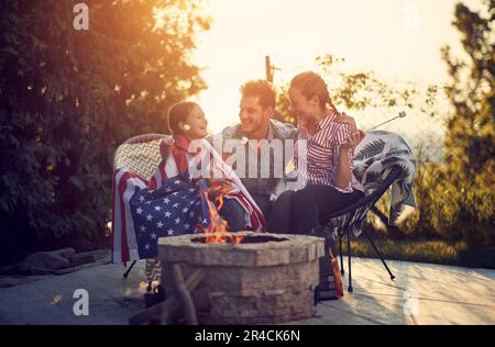 Eine Mutter, ein Vater und eine Tochter saßen um eine gemütliche Feuerstelle, ihre Gesichter strahlten vor Lachen und Freude. Im Geiste der Gelegenheit sind sie e Stockfoto