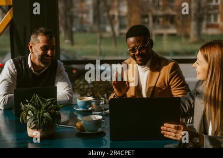 Nahaufnahme einer blonden Frau, die ihren Kollegen etwas auf dem Laptop zeigt, während sie im Café sitzt Stockfoto