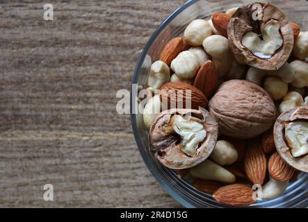 Walnusshälften und ganze Kerne verschiedener Nusssorten auf einem traditionellen Schneidebrett Stockfoto