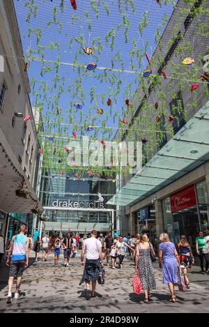 Der Eingang der Old Town Street zum Plymouth The Drake Circus Shopping Mall in Plymouth. Ein Netztuch mit Meeresmotiv sorgt im Sommer für Farbe und Schatten. Stockfoto