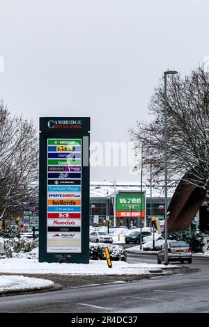 Ein Schild, auf dem alle Unternehmen und Geschäfte im Cambridge Retail Park an einem verschneiten Wintertag an der Newmarket Road, Großbritannien, aufgeführt sind. Stockfoto