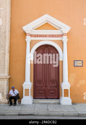 Ein Mann sitzt neben einer kunstvoll verzierten Tür in der Altstadt von Cartagena Colombia Stockfoto