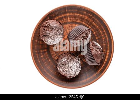 Vier hausgemachte Schokoladen-Cupcakes auf einer Tonschale auf weißem Hintergrund, Makro, Draufsicht. Stockfoto