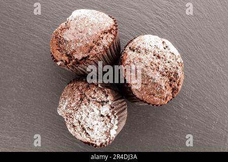 Drei hausgemachte Schokoladen-Cupcakes auf Schieferstein, Makro, Draufsicht. Stockfoto