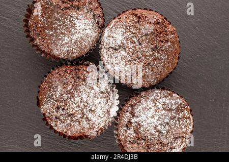 Vier hausgemachte Schokoladen-Cupcakes auf Schieferstein, Makro, Draufsicht. Stockfoto