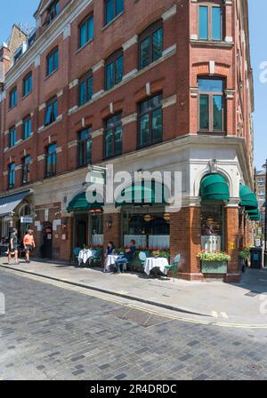 An einem sonnigen frühen Sommertag sitzen die Gäste an den Tischen vor dem Ivy Cafe und den St John Restaurants in der Marylebone Lane. London, England, Großbritannien Stockfoto