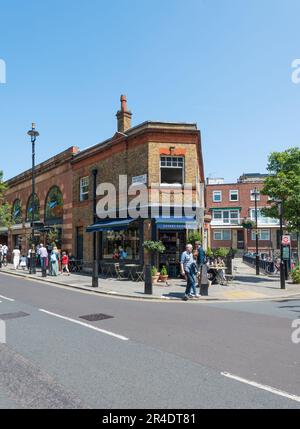 Leute, die an einem sonnigen Tag am französischen Restaurant Orrery in der Marylebone High Street vorbeikommen. Ein junges Paar, das draußen auf dem Bürgersteig sitzt. London, England, Großbritannien Stockfoto