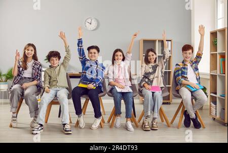 Glückliche Schüler sitzen in der Reihe und heben die Hand, um zu antworten Stockfoto