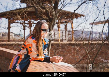 Junge Frau mit Sonnenbrille in einer bunten Jacke in Budapest Stockfoto