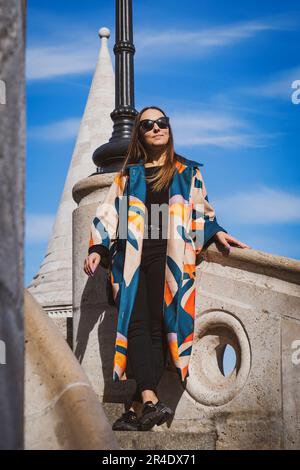 Junge Frau mit Sonnenbrille in einer bunten Jacke in Budapest Stockfoto