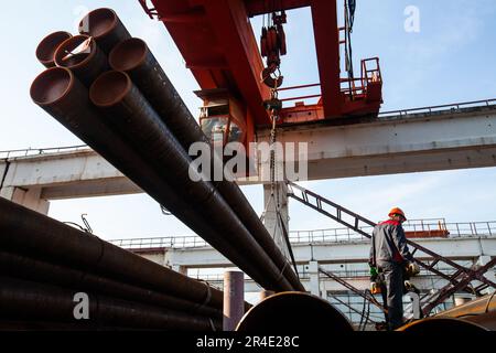 Podolsk, Provinz Moskau - 02. August 2021: Arbeiter laden Rohre mit einem Brückenkran. Stockfoto