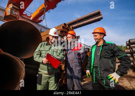 Podolsk, Provinz Moskau - 02. August 2021: Rohrlager. Ingenieur und zwei Arbeiter an Rohren mit großem Durchmesser im Hintergrund Stockfoto
