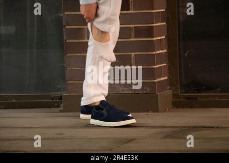 Ein Mann zieht kurze weiße Socken an und neben ihm stehen blaue Turnschuhe auf der Straße im Stadtzentrum, Mode und Style, Beine und Socken Stockfoto