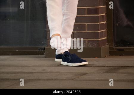 Ein Mann zieht kurze weiße Socken an und neben ihm stehen blaue Turnschuhe auf der Straße im Stadtzentrum, Mode und Style, Beine und Socken Stockfoto