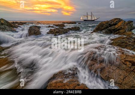 Ein Schiff Segelboot segelt entlang des Ozeans mit Einer Welle bricht an der Küste Stockfoto
